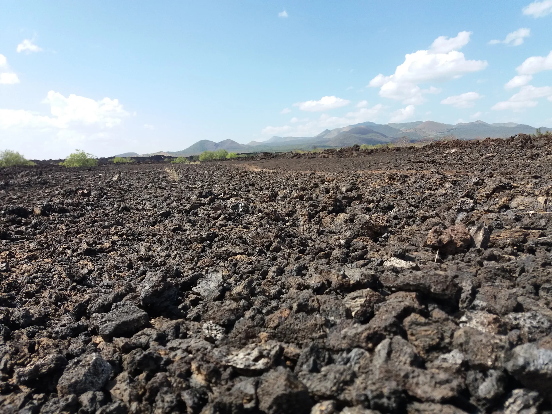 Dark rough lava across an open landscape with distant hills